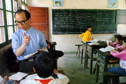 教师汪来九在为高年级的孩子上课，低年级的孩子在教室另一侧做作业。