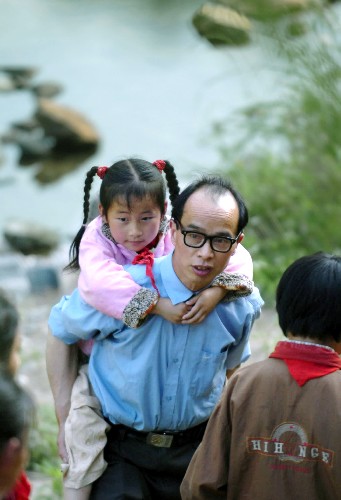 教师汪来九背着低年级学生走山路去上课。